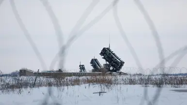 Op de linkerfoto opent luitenant Leon een deur van een groene werkcontainer. Op de rechterfoto is een Patriot-lanceerinrichting te zien door het prikkeldraad heen.