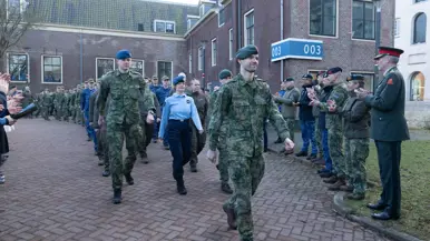  links: de staatssecretaris zit op een stoel. Rechts: Militairen lopen langs andere militairen