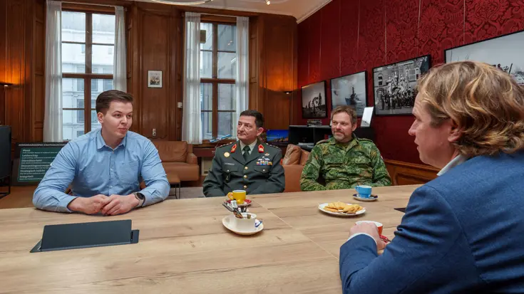 Defensiemedewerker zit aan tafel met 2 hoge militairen en de staatssecretaris.
