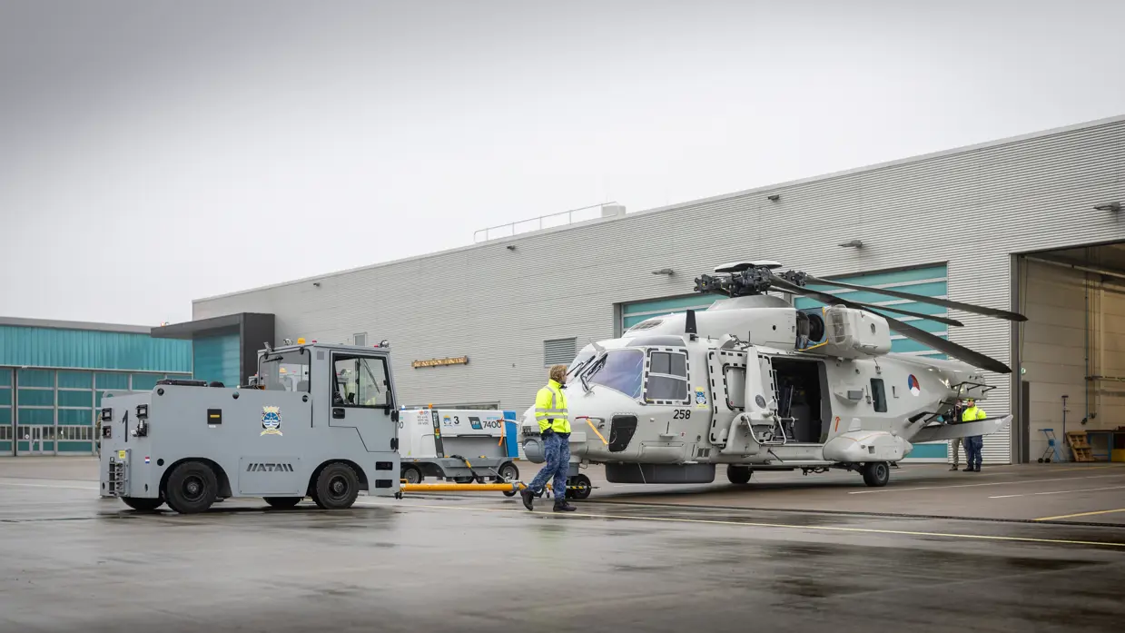 Een NH90 wordt door een tractor uit de hangar getrokken.  