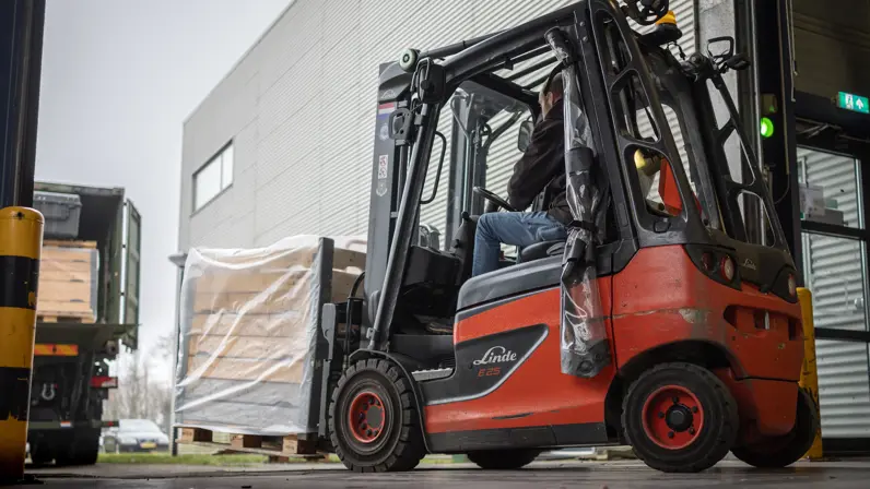 Een pallet wordt met een vorkheftruck in een groene vrachtwagen vanaf de zijkant ingeladen.