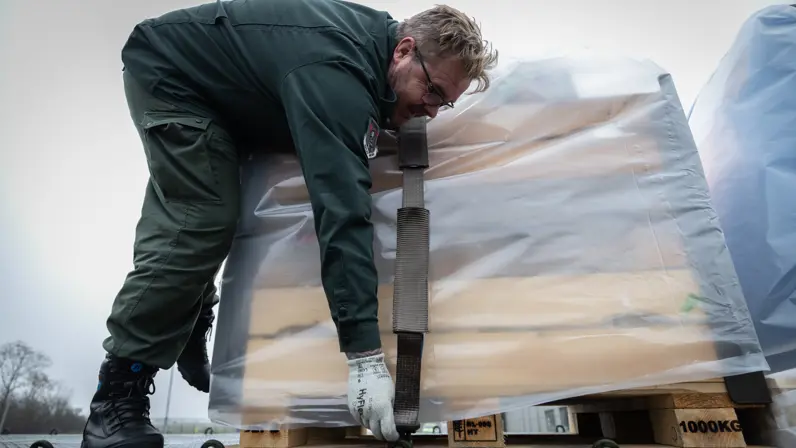 Een burgermedewerker plaats een spanband over de zijkant van een pallet.  