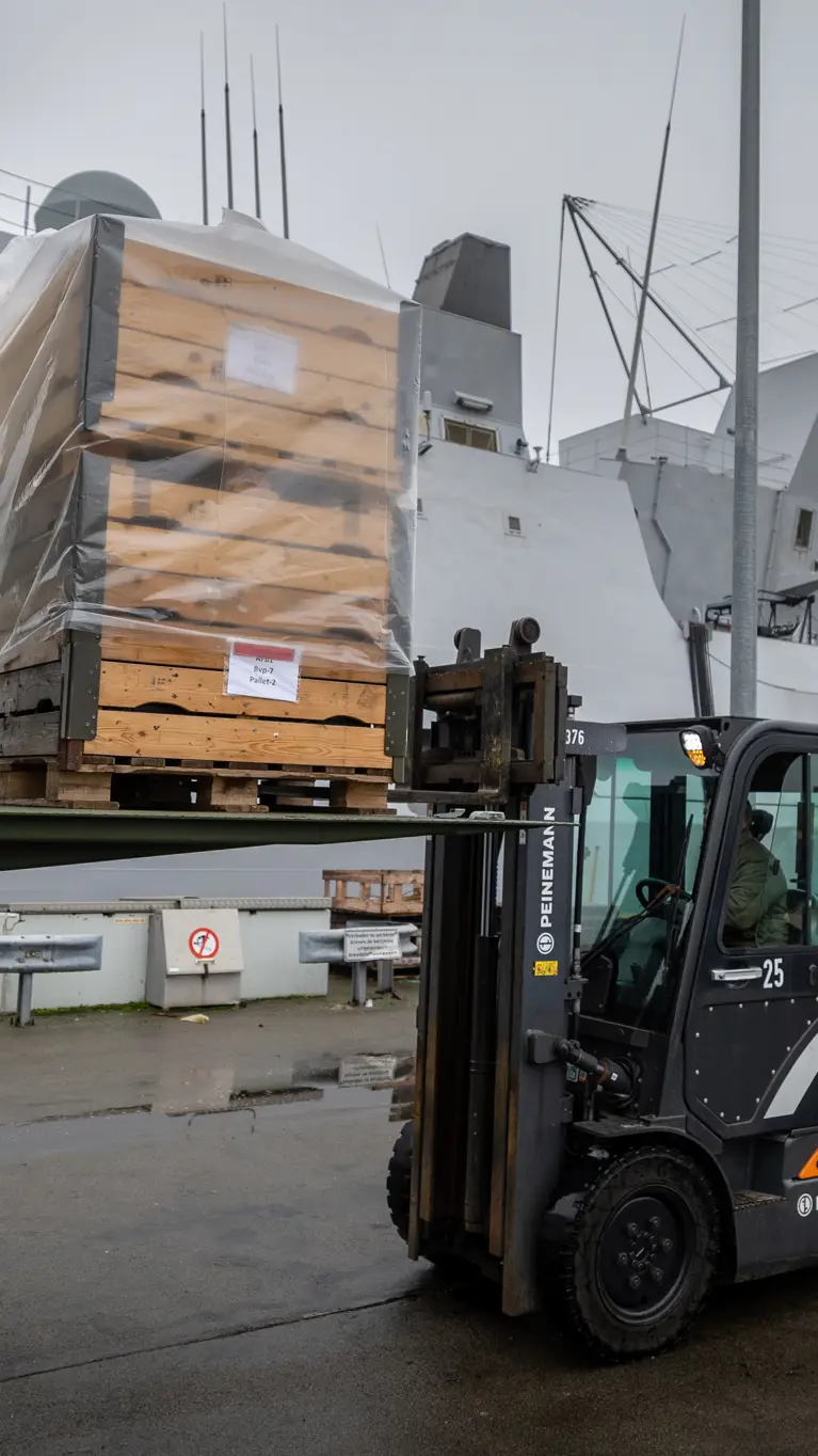 Een vorkheftruck die op de kade een pallet uit een vrachtwagen tilt.