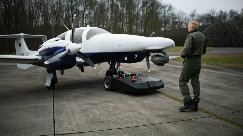Een wit klein vliegtuigje op een platform met ervoor een militair.