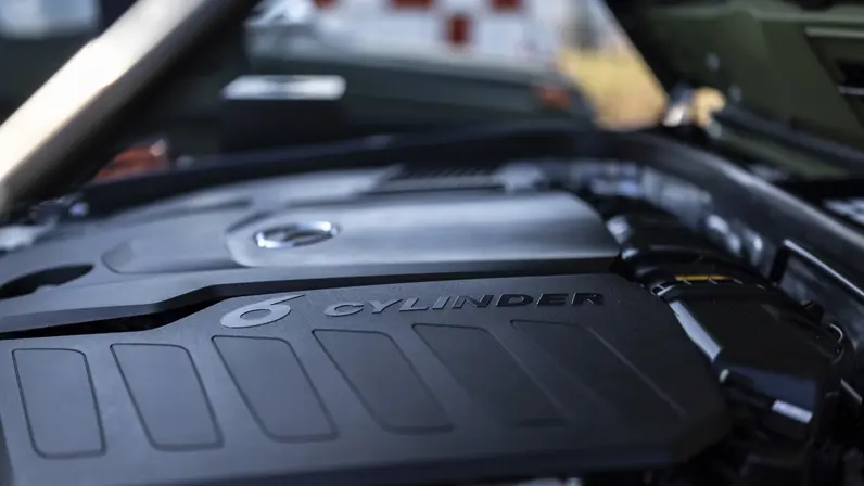 Het zijaanzicht van de motor met daarop een kunststof zwart dek, waarop ‘6 Cylinder’ staat.