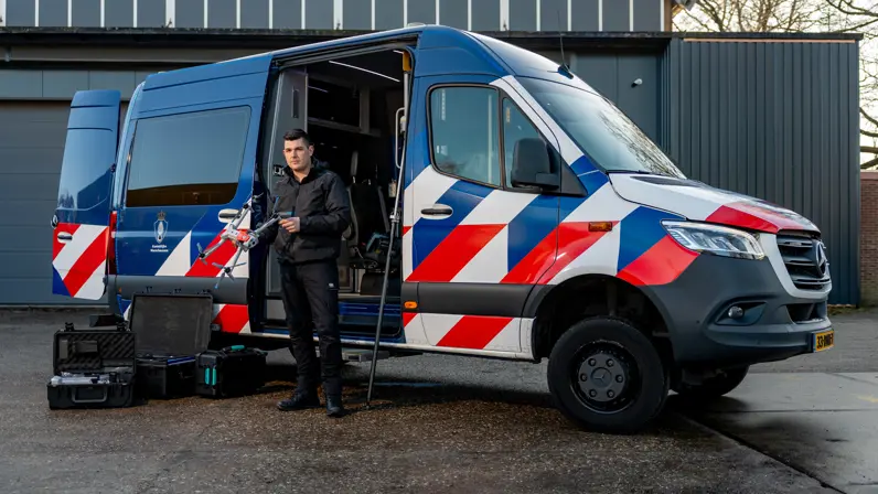 Adjudant Allard staat voor de dienstbus met een drone in zijn handen.