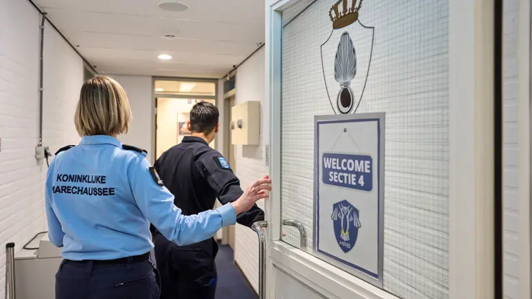 Adjudant Carolien en kapitein Tobias stappen door een deur waarop ‘Welcome Sectie 4’ wordt afgebeeld.