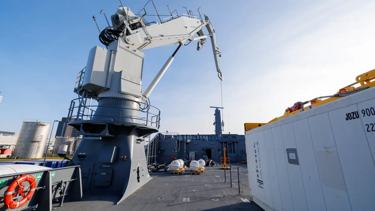Een grijze kraan op het dek van het schip, een donkergrijze reddingsboot en het predicaat met daarop ‘Den Helder’.