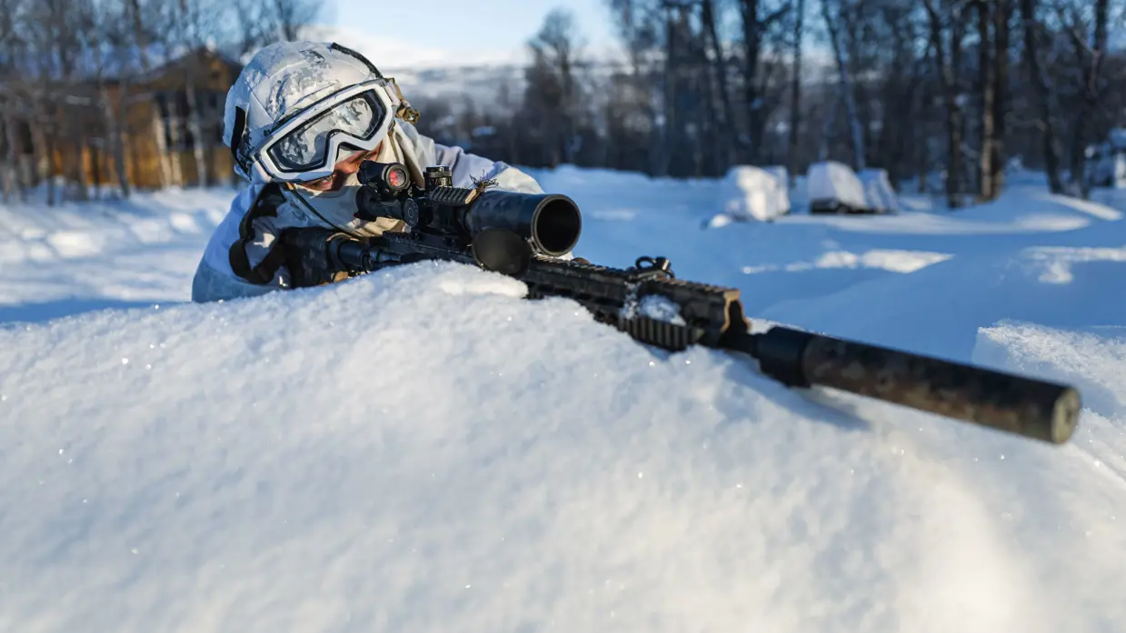 Een sniper richt zijn wapen van achter een sneeuwhoop.