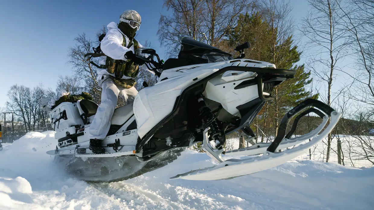 Foto links: een marinier rijdt met zijn sneeuwscooter tussen bosschages door. Foto rechts: een marinier komt met zijn sneeuwscooter los van de grond.