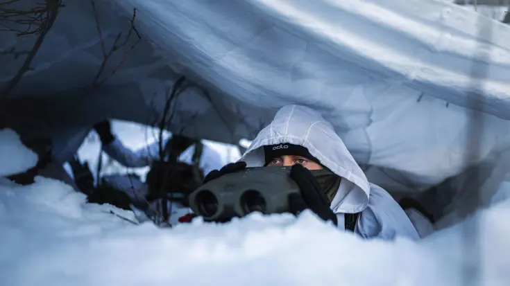 Een marinier met verrekijker onder wit zeildoek in de sneeuw.