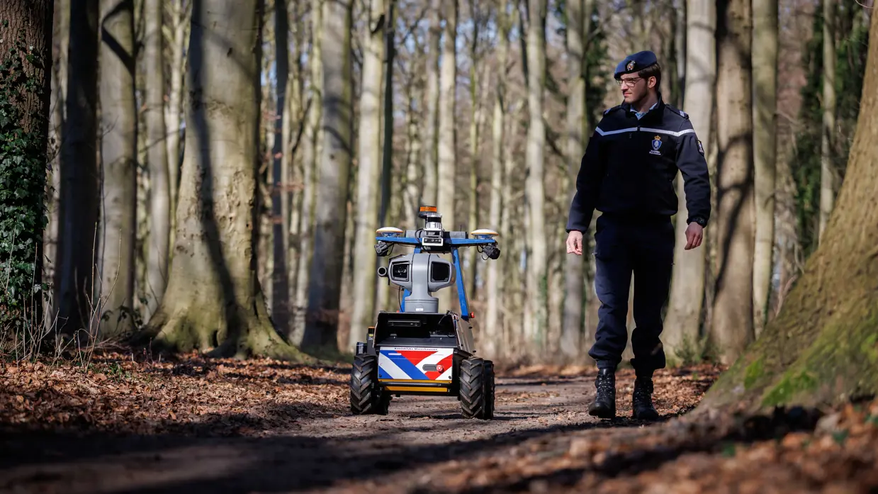 Een marechaussee loopt samen met de Roboguard door het bos.