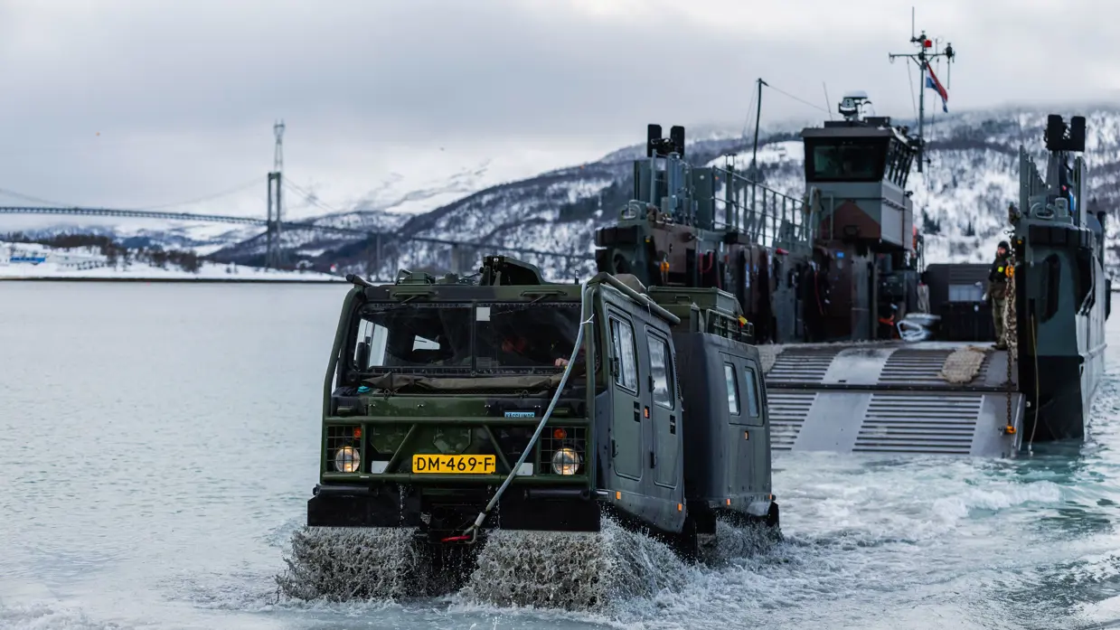  Een amfibisch voertuig rijdt vanaf een landingsvaartuig het water in van een besneeuwd Noors fjord.