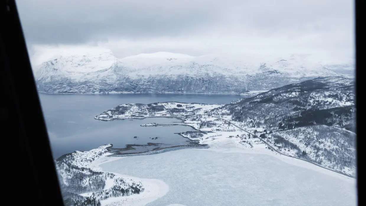 Een sneeuw- en ijsvlakte grenzend aan een fjord, gezien vanuit een helikopter.