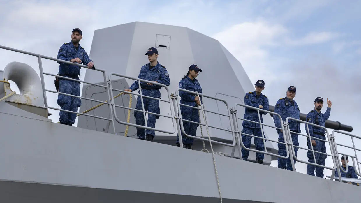 Links: Bemanningsleden bij de reling, met het scheepskanon op de achtergrond. Rechts: bemanning aan boord. Een van hen heeft een koptelefoon vast. 