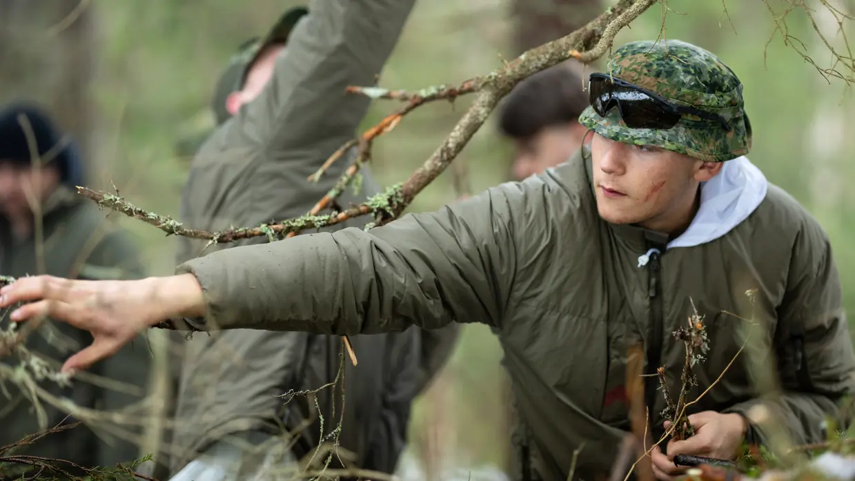 Soldaat Nathan sprokkelt in het bos brandbaar materiaal voor een vuurtje. 