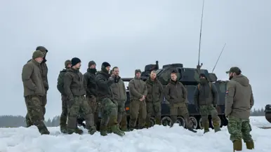 Manschappen krijgen in de sneeuw een evaluatie over de oefening, met op de achtergrond een CV90.