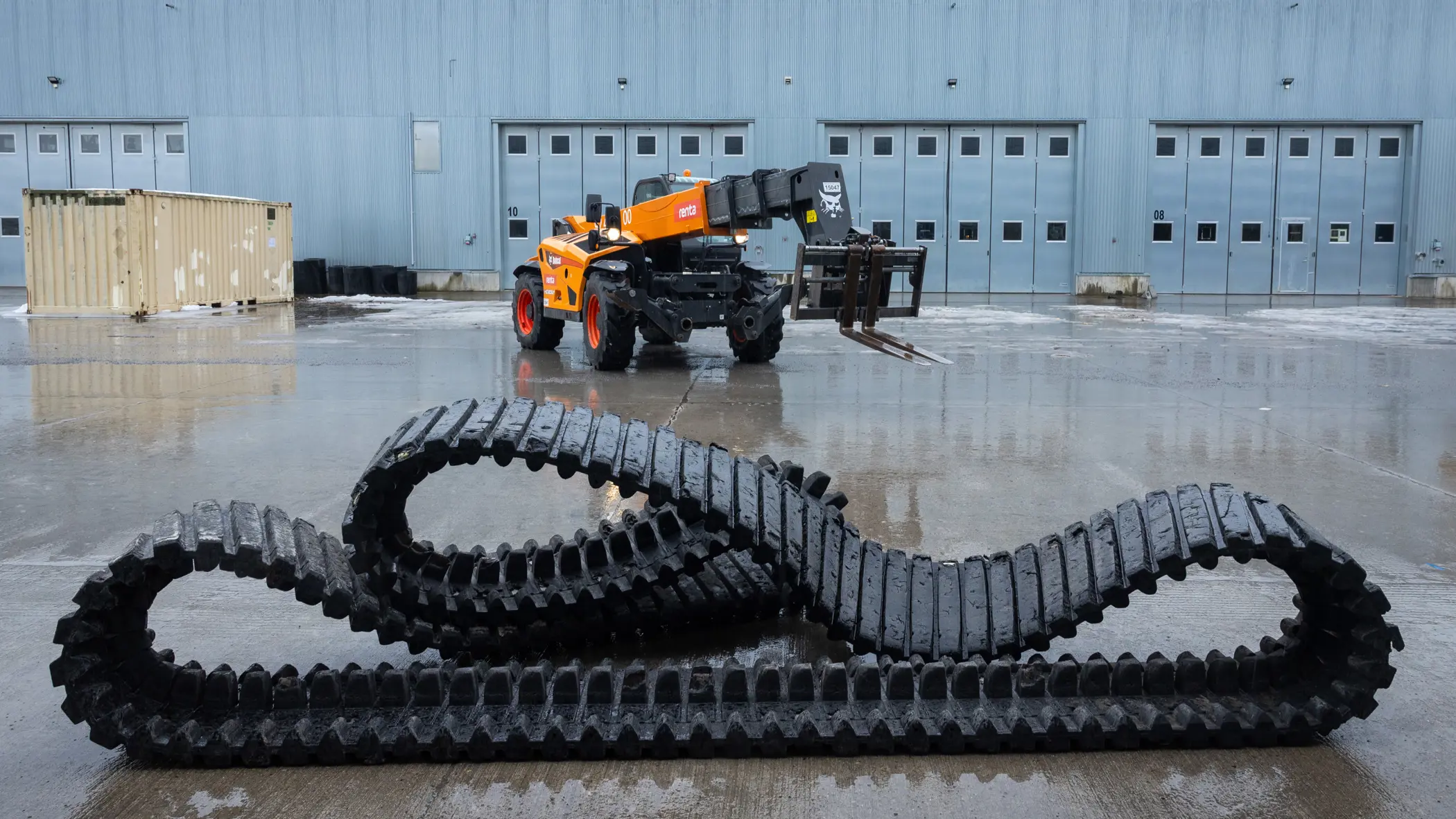 Een grote rubberen band ligt op de grond, erachter staat een kraanwagen. 