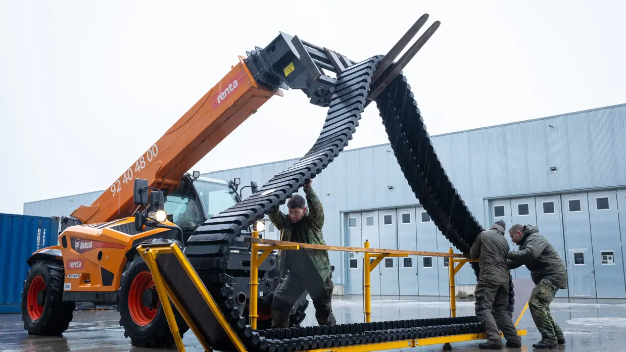 Links: een versleten rubberen band track, rechts: met een heftruck wordt een rubberen band track omhoog gehesen.