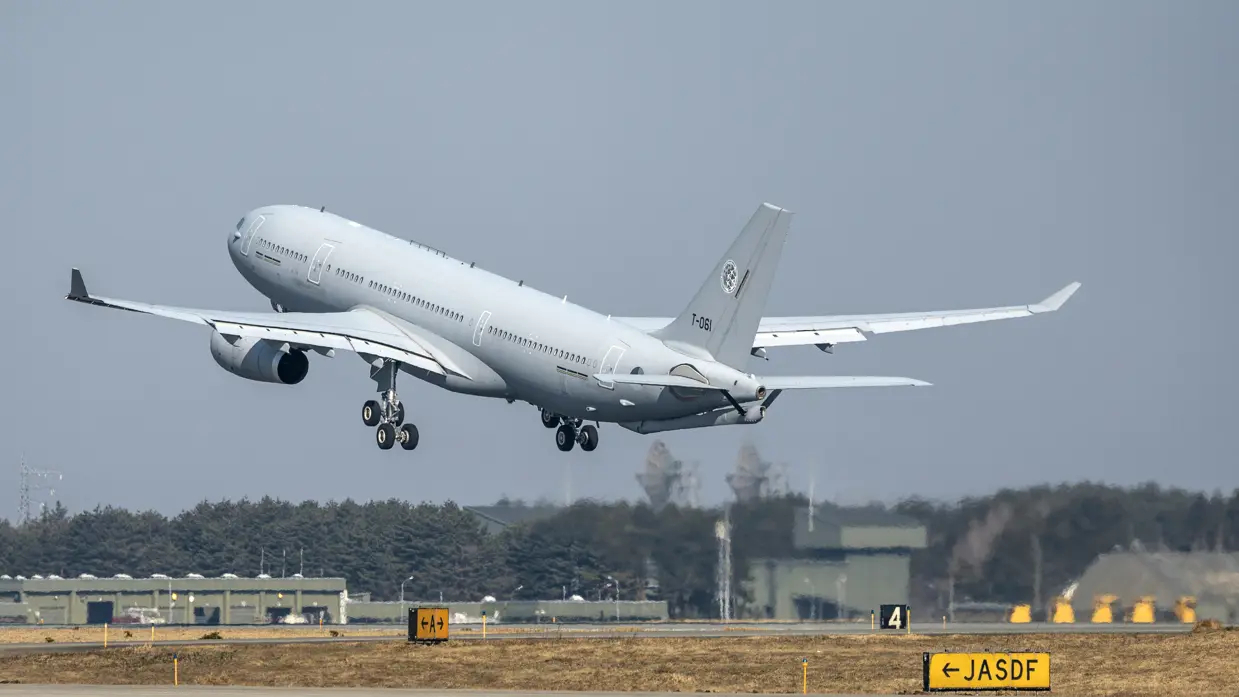 Een A330 MRTT stijgt op. In de achtergrond zijn hangars en radartorens te zien.
