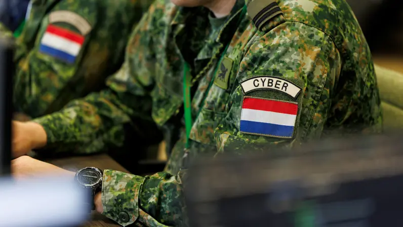 Militair met een cyber patch op zijn linkerarm aan het werk achter een computer.&nbsp;