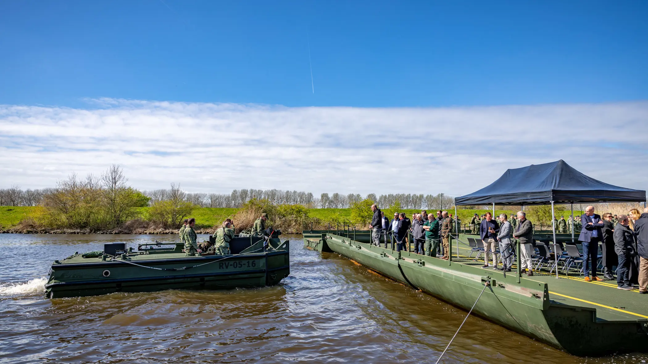 Nieuwe brugslagcapaciteit ligt over een rivier. Daarnaast vaart een boot met militairen.