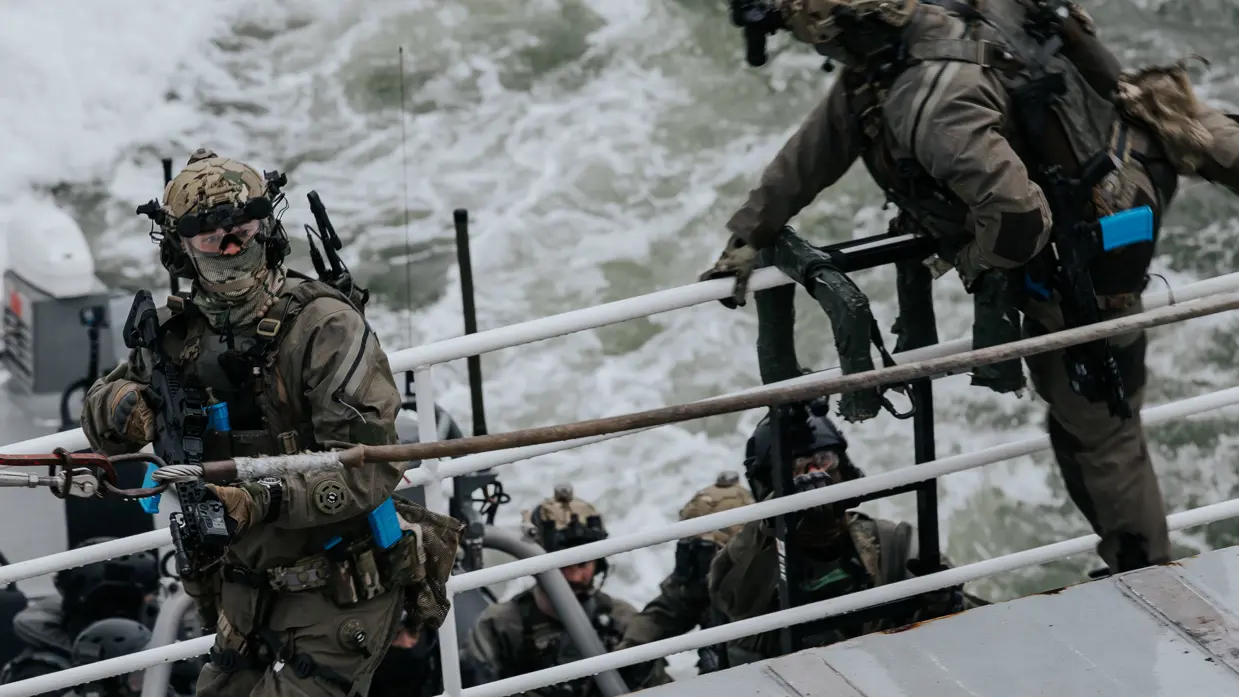 Op de linkerfoto klimt een militair aan boord, terwijl een collega dekking geeft. Rechts hangt een blauwe politiehelikopter stil boven het schip om operators af te zetten aan boord.