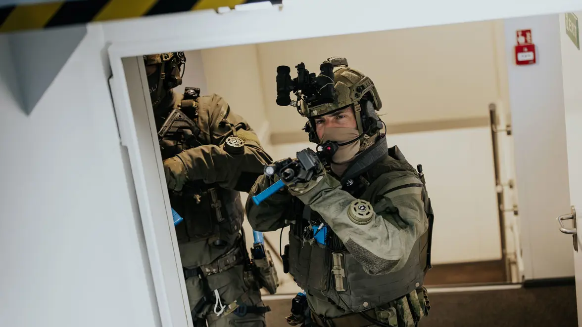 Een operator van NLMARSOF staat in een trapgat en kijkt over een dek, wapen in de aanslag. Een collega staat klaar om achter hem aan te komen. 