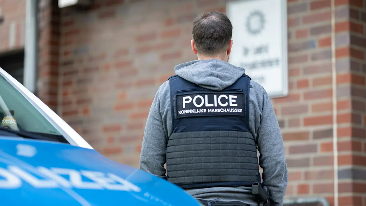 Een Nederlandse marechaussee op de rug gefotografeerd bij een Duits politiebusje.
