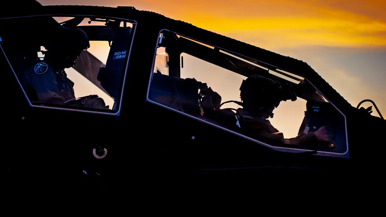 Een militaire helikopter staat stil in een veld, terwijl twee soldaten bij een groene terreinwagen met open laadbak staan. Rechts: het interieur van een helikopter tijdens zonsondergang. Twee piloten zitten in de cockpit, omlijst door oranje en donkere kleuren aan de lucht. 