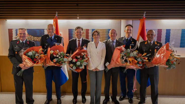 Minister van Defensie staat tussen aantal gedecoreerden die bloemen vasthouden.