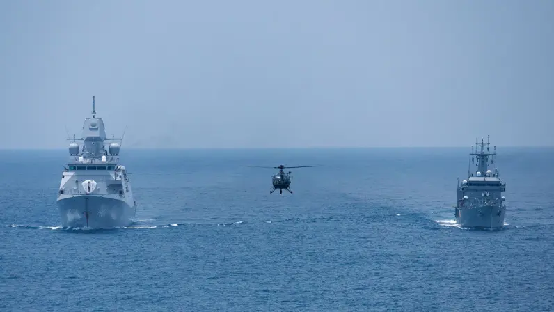 Zr.Ms. De Ruyter op volle zee, samen met een buitenlands marineschip en een helikopter.