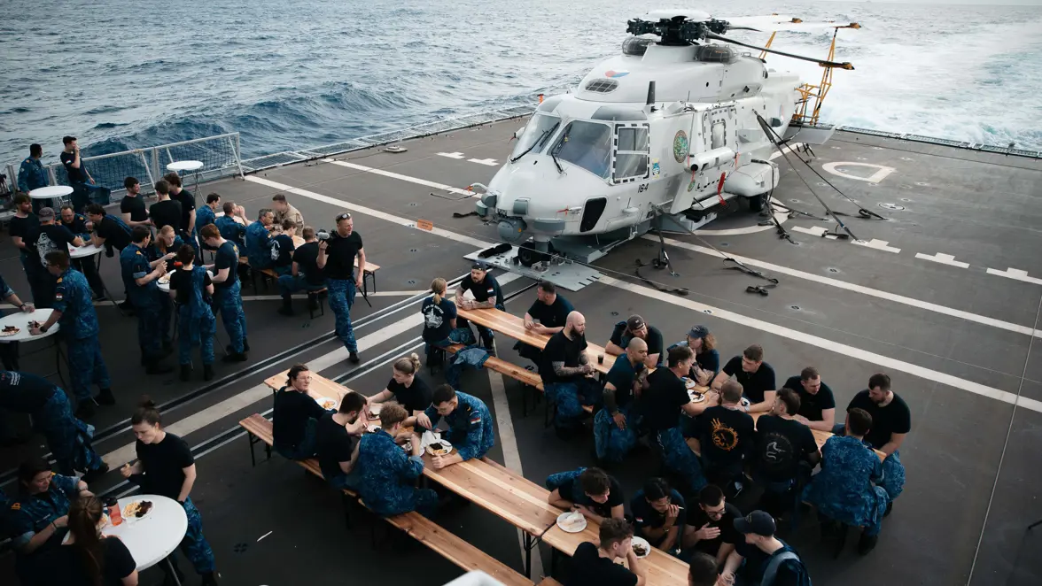 Bemanningsleden zitten aan lange tafels op het helidek, voor de NH90-boordhelikopter.