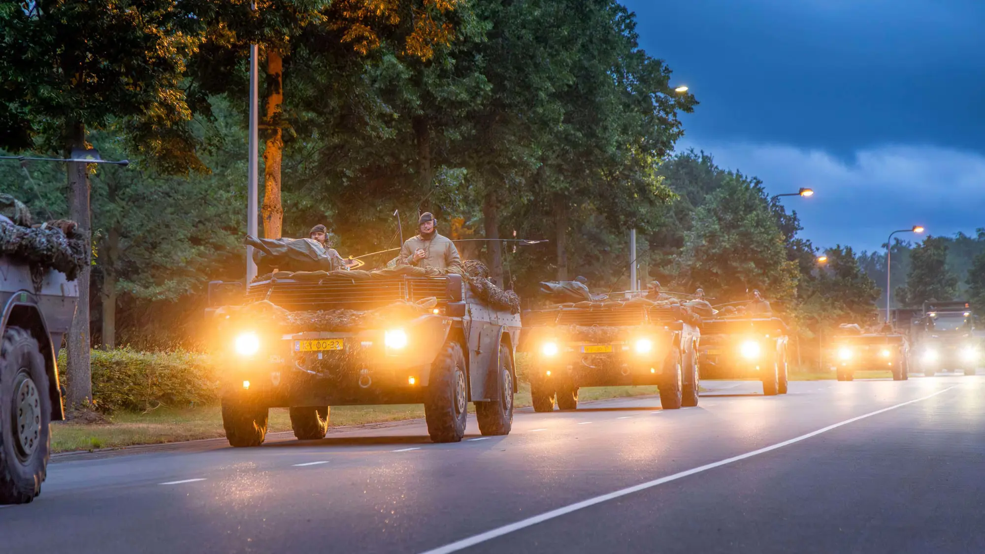 Militaire colonne rijdt met verlichting aan over de openbare weg.