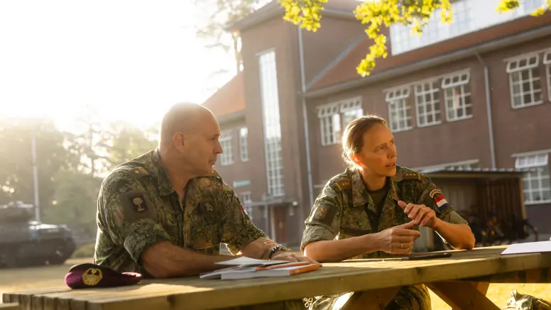 AOO Michel Vonk en kolonel Kim Schreuder zitten buiten aan een houten tafel.