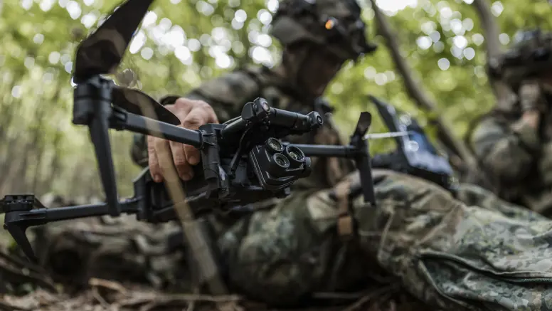 Een militair houdt zittend een drone in de hand en kijkt op z’n monitor.