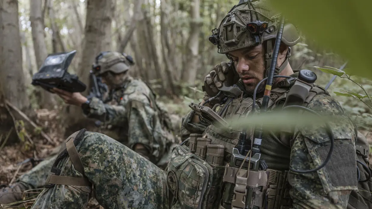 Een militair praat via de radio, op de achtergrond zijn collega.