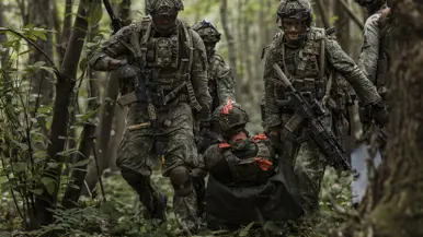 Een groep soldaten sleept een gewonde oefenvijand op een provisorische brancard door het bos.