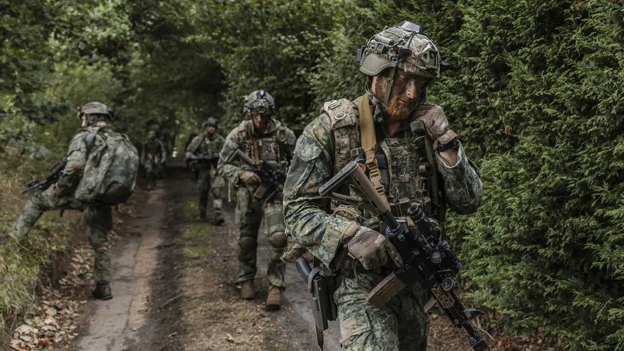Een groep militairen komt uit het bos gelopen.