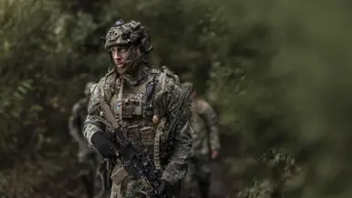 Een militair loopt door het bos en scant de omgeving.