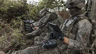 Een militair plugt een kabel in een powerstation, terwijl z’n collega op het scherm kijkt.