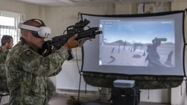Een militair met een VR-bril voor een scherm waarop hij ‘mee schiet’.