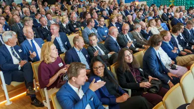 Een militair speelt op een keyboard met achter zich een groot projectiescherm en een commandeur spreekt een zaal toe met achter zich een groot projectiescherm.
