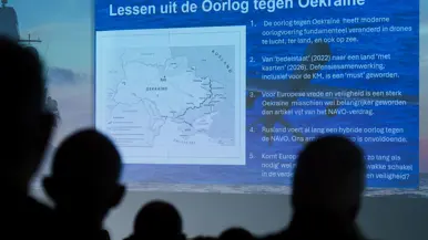 Een oplopende zaal vol aanwezigen en een videoscherm met daarop de lessen uit de oorlog tegen Oekraïne.