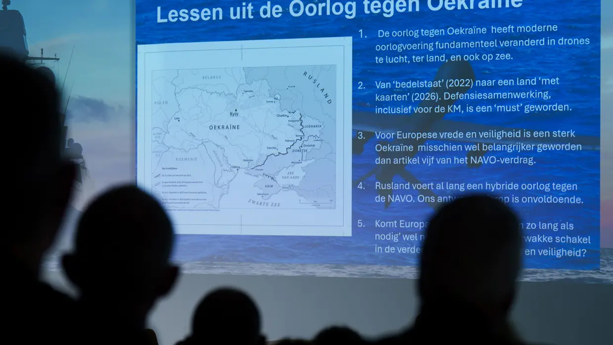 Een oplopende zaal vol aanwezigen en een videoscherm met daarop de lessen uit de oorlog tegen Oekraïne.