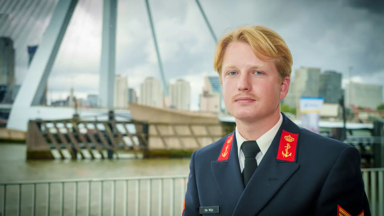 Jonge militair in tenue 6 poseert voor water en een hoge brug. 