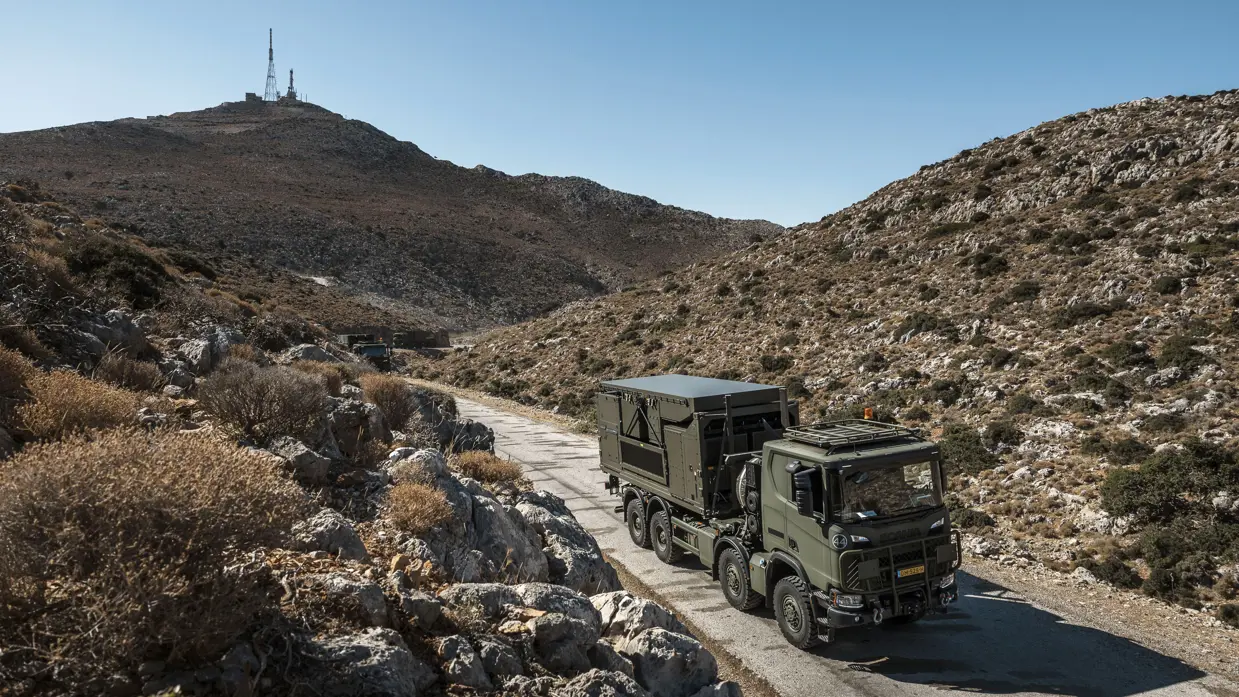 Een militaire vrachtwagen met de ingeklapte radar achterop rijdt door een heuvelig landschap op Kreta.