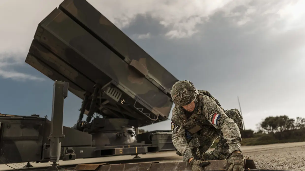 Een vrouwelijke militair legt knielend de laatste hand aan de plaatsing van een NASAMS-wapensysteem dat op de achtergrond is te zien.