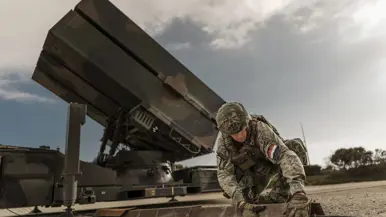 Een vrouwelijke militair legt knielend de laatste hand aan de plaatsing van een NASAMS-wapensysteem dat op de achtergrond is te zien.