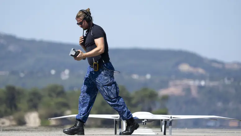Een marinecollega loopt langs een drone die op de startbaan staat.